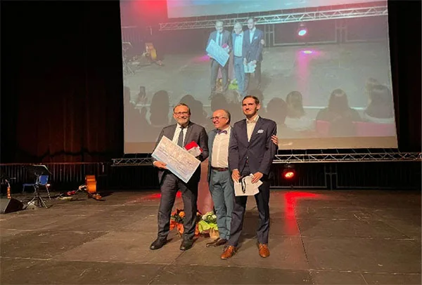 Trois hommes posent sur une scène avec un prix.