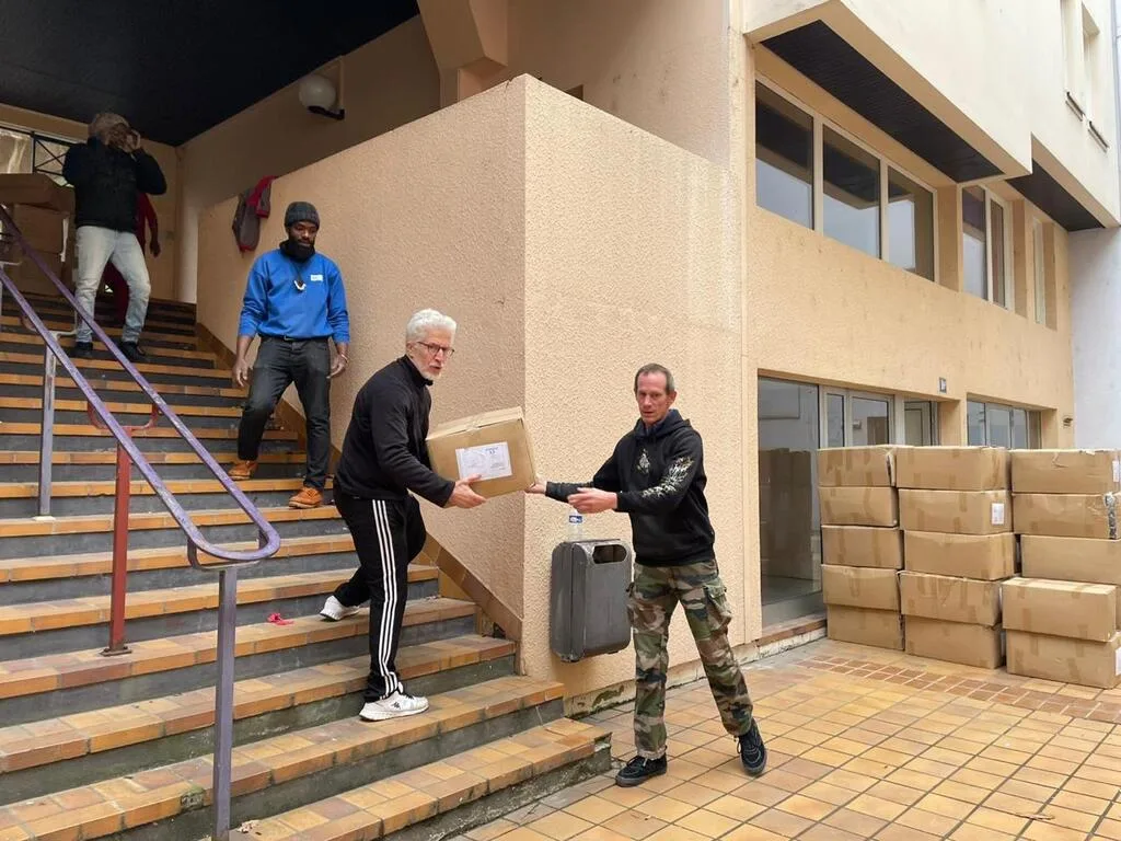 Personnes transportant des cartons devant un bâtiment.