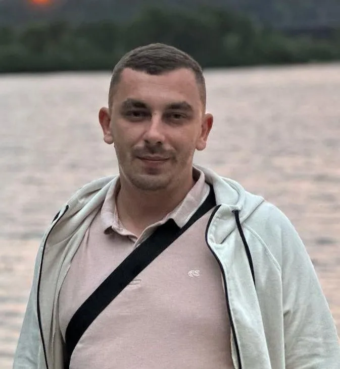 Homme souriant devant lac au coucher du soleil.