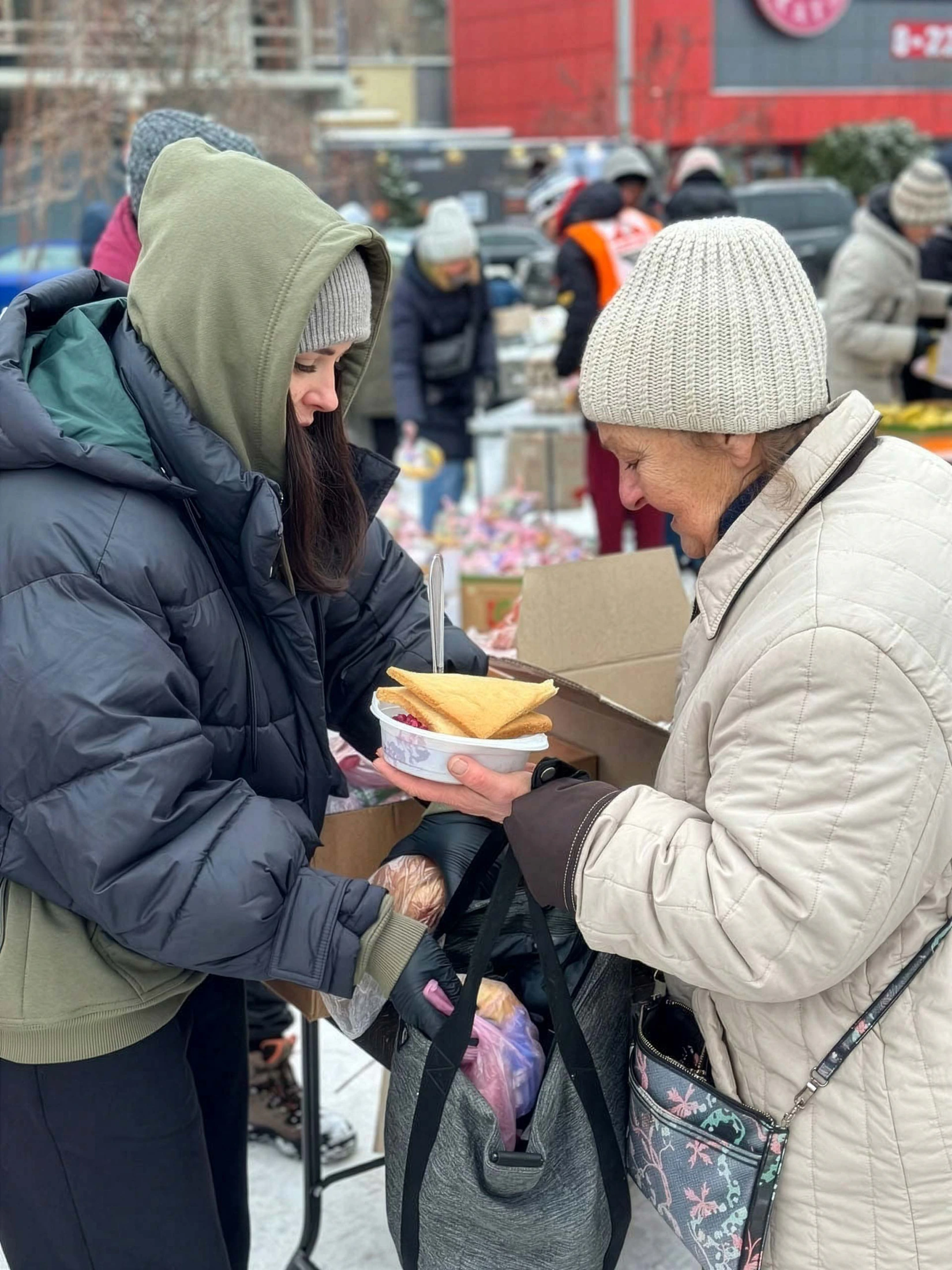 Une bénévole remet un repas chaud et du pain à une femme âgée lors d'une distribution alimentaire, en hiver.