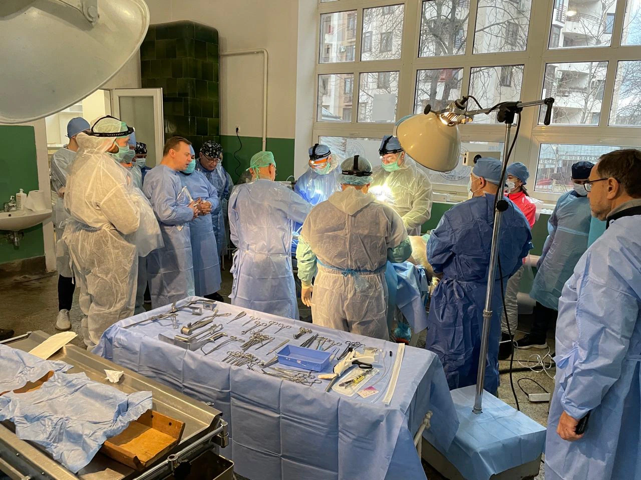 Séance de formation à la chirurgie de guerre : une quinzaine de soignants en tenue stérile autour de la table d'opération, instruments préparés au premier plan.