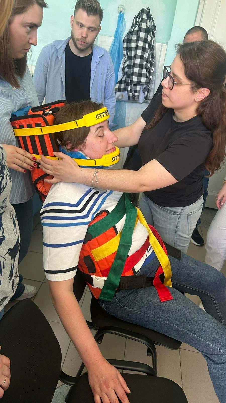 Séance de formation : une soignante pose un collier cervical et une attelle de rachis à une participante, devant un groupe de stagiaires.