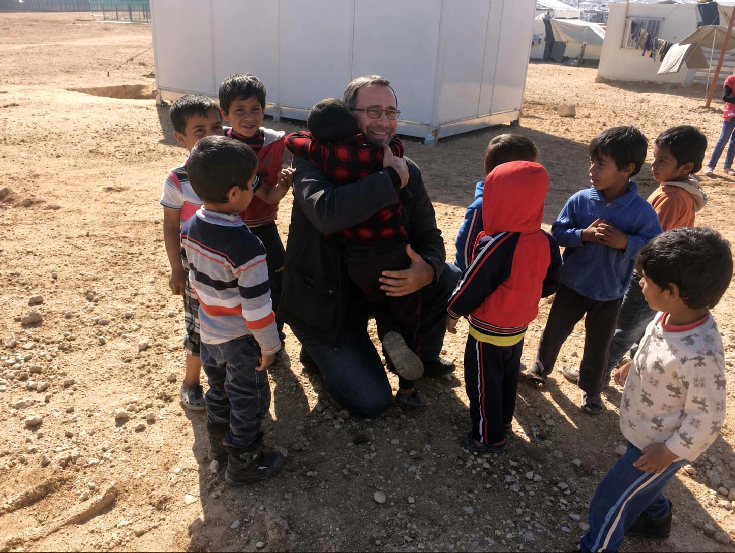 Un intervenant de HuSoMe, accroupi, serre un enfant dans ses bras, entouré d'une dizaine d'enfants dans un camp de déplacés.
