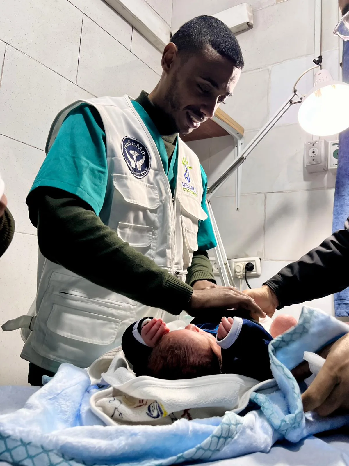 Un soignant s'occupe d'un nouveau-né emmailloté, sous une lampe d'examen.